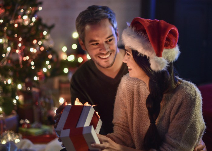 portrait of a young couple in their living room in  christmas eve the young woman with santa hat on head smiled in opening his gift, a lit Christmas tree in the background